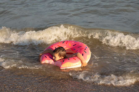 A cheerful boy 5 years old swims in the sea on an inflatable ring in the form of a donut on a sunny...