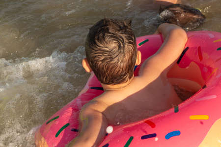 A 5-year-old boy is swimming and having fun in the sea near the shore with a donut-shaped inflatable circleの写真素材