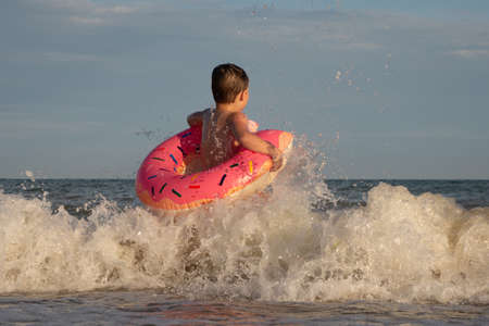 A 5-year-old boy is swimming and having fun in the sea near the shore with a donut-shaped inflatable...