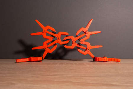 Clothespins, carpentry clamps of orange color lie on a wooden table. A pyramid in the form of a...