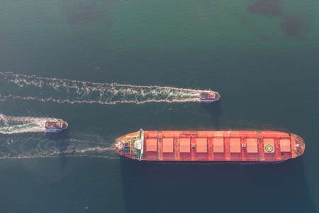 The dry cargo vessel enters the port with the help of tugs. Photo from a helicopter. Bird's-eye viewの写真素材