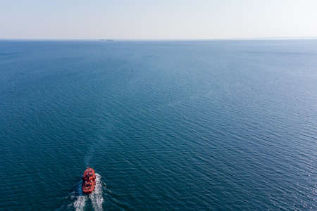 The pilot boat orange goes to meet the vessel on the outer roads. Helicopter view. Top view of the seaの写真素材
