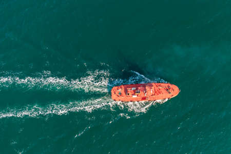 The pilot boat orange goes to meet the vessel on the outer roads. Helicopter view. Top view of the seaの写真素材