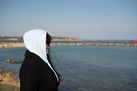 Brunette woman in a black coat with a white hood on the background of the seaの写真素材