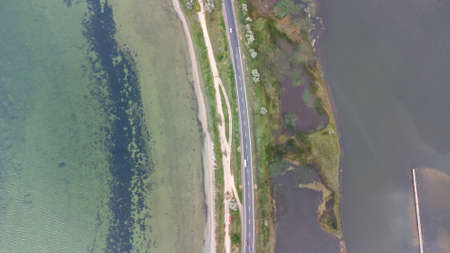 A highway that runs along a narrow spit between the sea and the estuary. Cars on the road. Aerial...