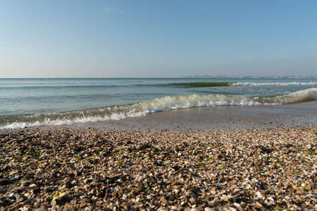 Sea waves running on a sandy shore on a clear sunny day. City in the background