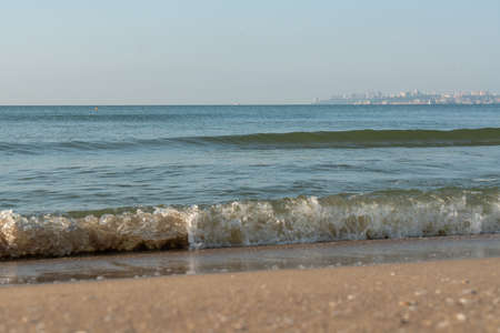 Sea waves running on a sandy shore on a clear sunny day. City in the background