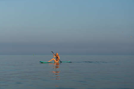 Girl with a paddle. Young blonde woman on a sup board in the sea at sunset