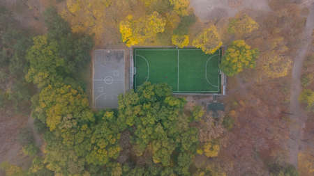 Football field with green grass and basketball court in city park in autumn. Leaf fall in the park. Aerial viewの写真素材