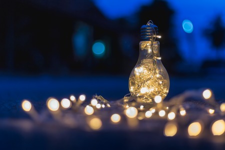 Garland lights in a glass jar like a light bulb on the street at night with a blurry background.の写真素材
