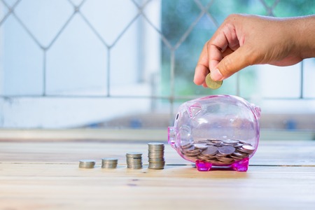 Pink piggy bank with a medal placed in front pile. There are men's hands are coin , The concept of...