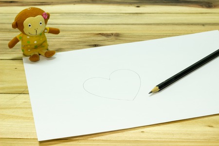 Write a heart White paper, monkey doll and pencil on wooden deskの写真素材