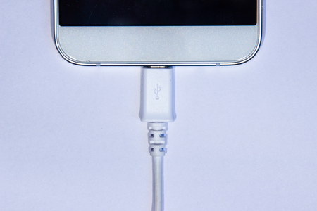 Cell phone plugged in data transfer cable on a white background.