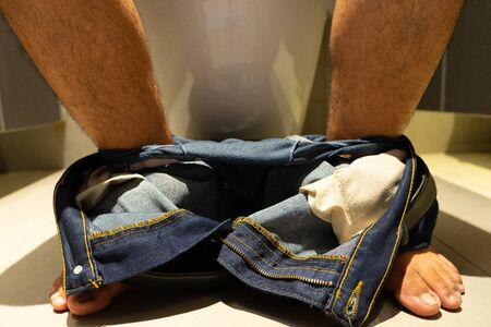 Men's legs take off jeans, sit in the bathroom.の写真素材