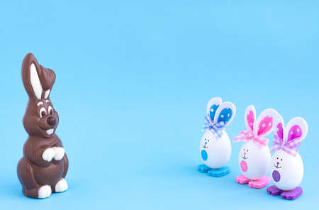 Chocolate rabbit and three Easter eggs with painted eyes and rabbit ears on a blue background...