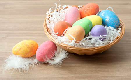 Easter colorful eggs in a wicker basket on a wooden brown table. Krypny plan. Soft focus.