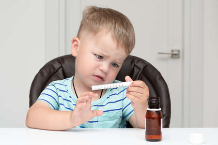people. A small handsome caucasian boy in a striped turquoise t-shirt sits at a white table and...