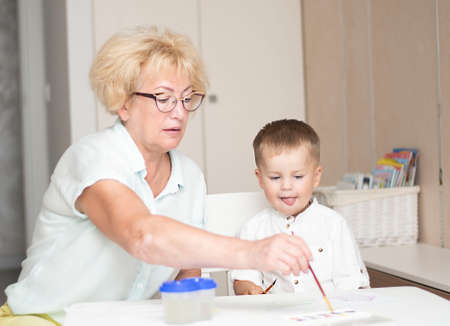 Caucasoid woman and little boy draw with paints at the table in the home interior. Family concept.の写真素材