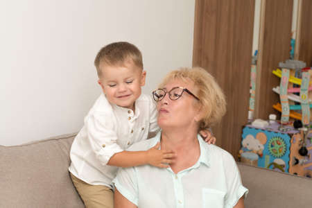 Happy and beautiful caucasian grandmother and little grandson are hugging while sitting on the...