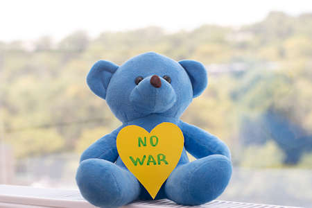 Concept. Childrens soft toy, a blue teddy bear with the inscription no war on the background of the window.の写真素材