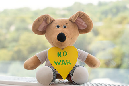 Peace concept. Childrens soft toy, a beige plush mouse with the inscription no war on the background of the window.の写真素材