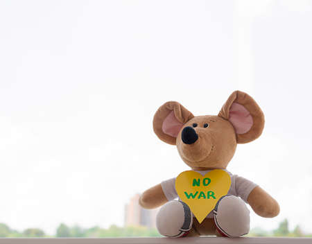 Peace concept. Childrens soft toy, a beige plush mouse with the inscription no war on the background of the window.の写真素材