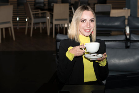 People. A beautiful Caucasian blonde girl sits in a cafe with a cup of coffee and communicates...