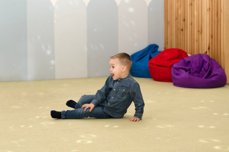 Children. A handsome little caucasian boy is sitting on the floor in the childrens room at a holiday party and making funny faces.の写真素材