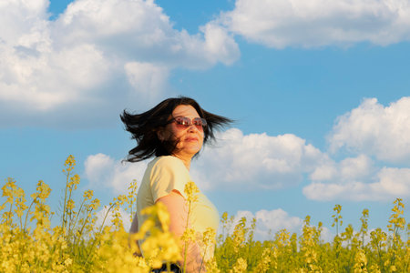 A beautiful girl in sunglasses stands in a field of yellow flowers against a blue sky, smiles happily and inhales the fresh spring and clean air. Peace concept. The color of the flag of Ukraine.の写真素材