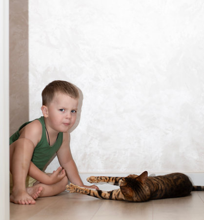 A little boy of 4 years old has fun playing with a red, leopard bengal cat on the floor in a home interior.の写真素材