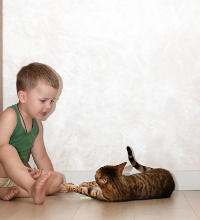 A little boy of 4 years old has fun playing with a red, leopard bengal cat on the floor in a home interior.の写真素材