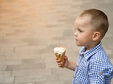 The boy eats ice cream. A beautiful, Caucasian, fair-haired boy, 4 years old, cheerfully and emotionally licks ice cream in a waffle cup with his tongue on the street in summer. Close-up.の写真素材