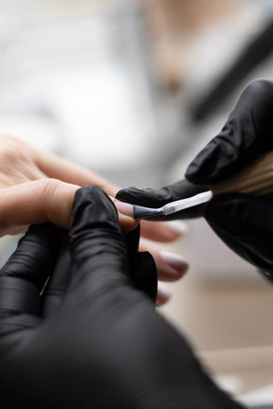 Beauty concept. A manicurist in black latex gloves makes a hygienic manicure and paints the clients nails with gel polish in a beauty salon. Close-up.の写真素材
