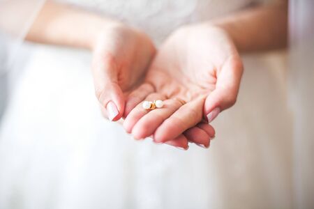 White earrings in the beautiful and gentle hands of the bride, dressed in a wedding snow-white dressの写真素材