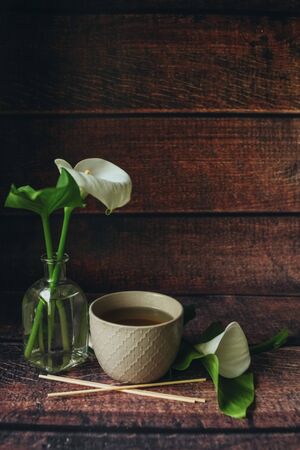 A light beige large ceramic cup stands on a dark wooden table, black hot tea is poured in it, a beautiful breakfast with an unusual white flower calの写真素材