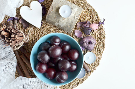 Ripe plums in bowl on tablecloth in a rustic setting. Composition with plums, candles, table cloth, fragrant wood sticks and heart.View from above.の写真素材
