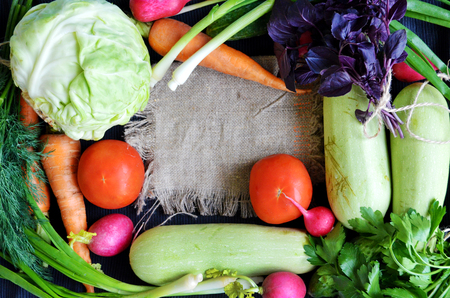 Fresh vegetables and greens in bunches arranged in a frame on a background of a dark tablecloth and burlap with space for text. View from above.の写真素材