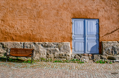 An ancient textured wall with a stone basement, a blue door and a bench. Bright concept.の写真素材