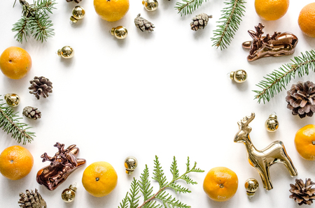 Christmas frame with golden deers, mandarins, fir branches, New Year balls and conesona white background. Christmas background for presentation of work or text. Top view. Copy spaceの写真素材