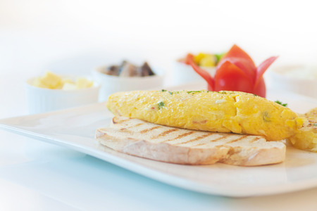 Omelette or scrambled egg served with hash-brown and tomato, on white.