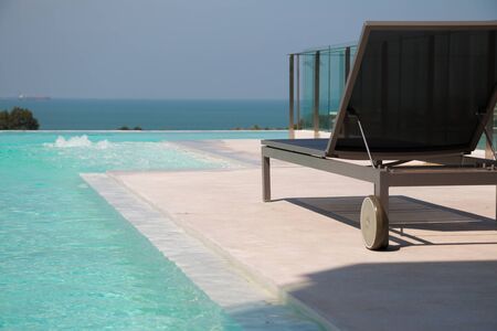 sunbed with infinity pool on the building, and blurred seascape background.