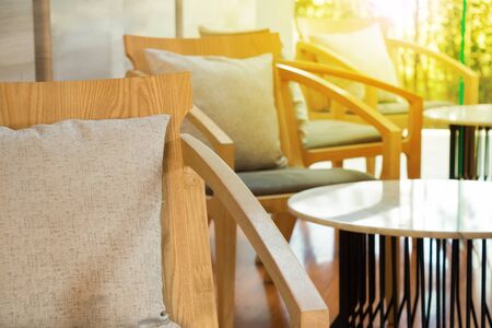 Morning light in lobby lounge with wood armchairs and round tables in modern residential building.