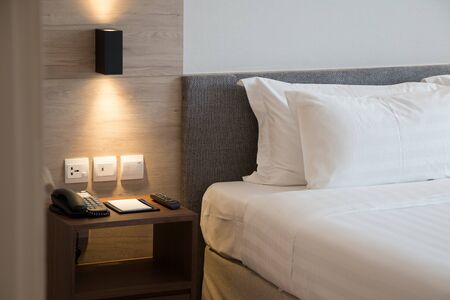 Modern interior hotel bed room with simply soft headbord and telephone ,tv remote on side table.
