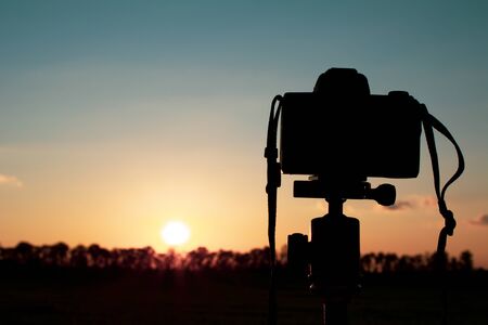 silhouette of a camera on a tripod that shoots a red sunset on the lawnの写真素材