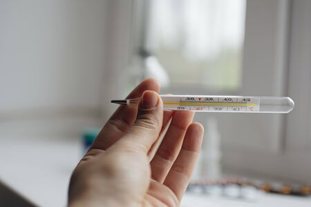 medical thermometer in hand on the background of a first aid kit and various pillsの写真素材