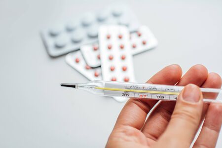 medical thermometer in hand on the background of a first aid kit and various pills