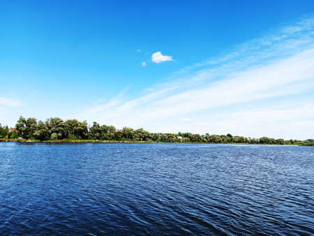 Beautiful landscape, water surface of the river, blue sky with white clouds and forest in the...