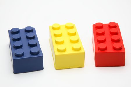 Three plastic interlocking building blocks - blue, yellow, and red - sitting on a white surface. Horizontal shot. Isolated on white.の写真素材