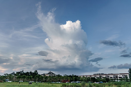 Clouds in the blue sky over the green grass field and buildings, A thick cumulonimbus cloud that is...