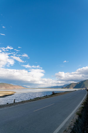 Winding road on the lake shore under a blue sky with cloudsの写真素材